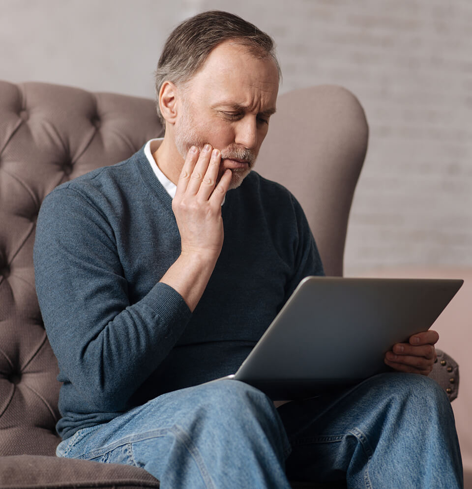 man holding his jaw in pain while looking at his laptop